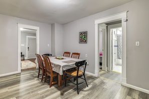 A dining area with a table set for four, surrounded by wooden chairs, a framed botanical print on the wall, and a bathroom visible through an open door. - 2 Mi to State Park! Cozy Apt Near Niagara Falls (Niagara Falls)
