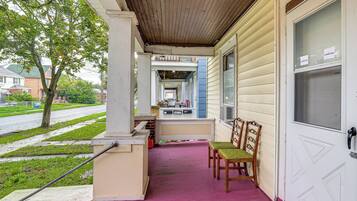 A porch with a pink floor, a bench, and chairs. There is a door with a window and a sign indicating 'LOWER UNIT'.