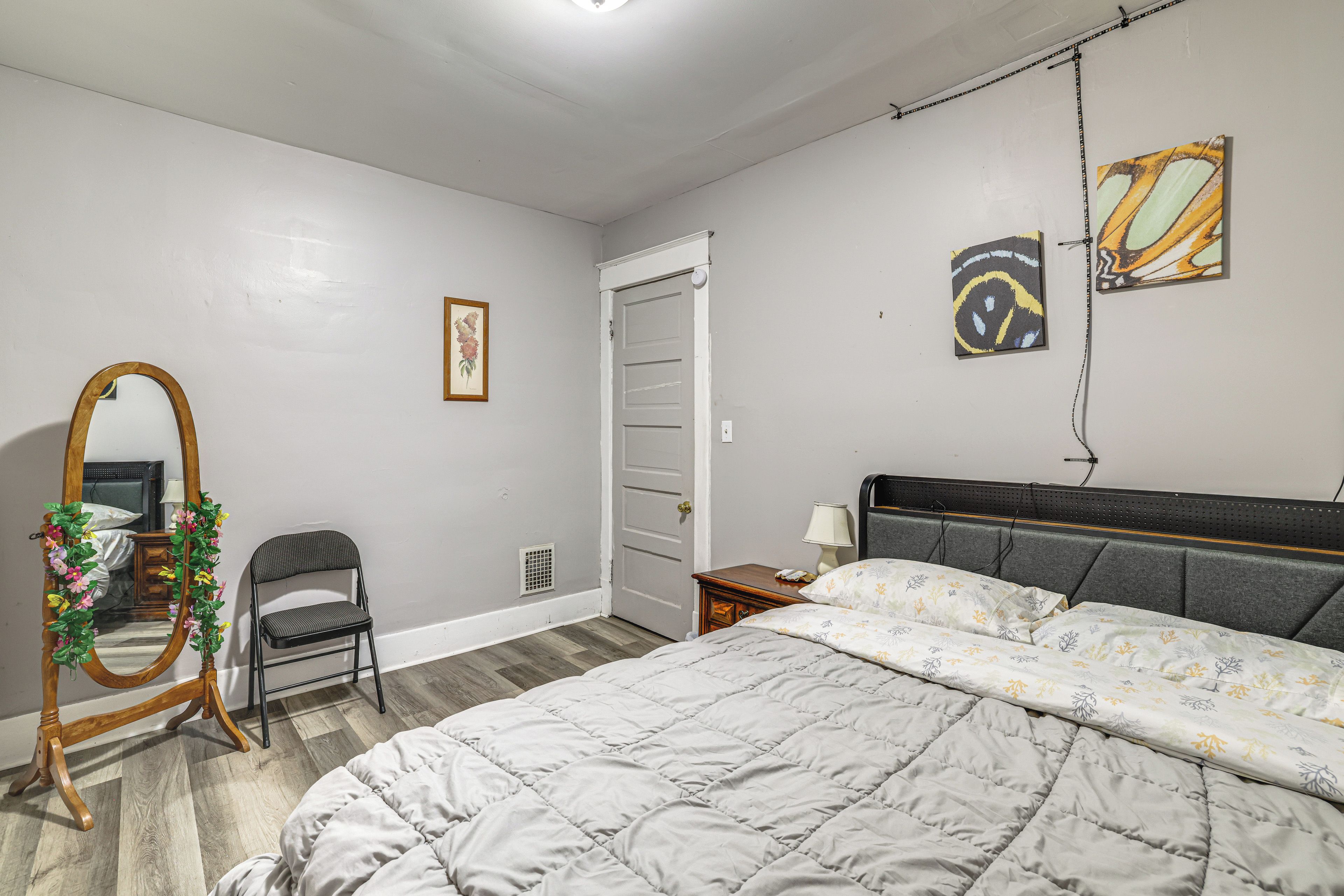 Un dormitorio con cama, una silla, cómoda, espejo y puerta.