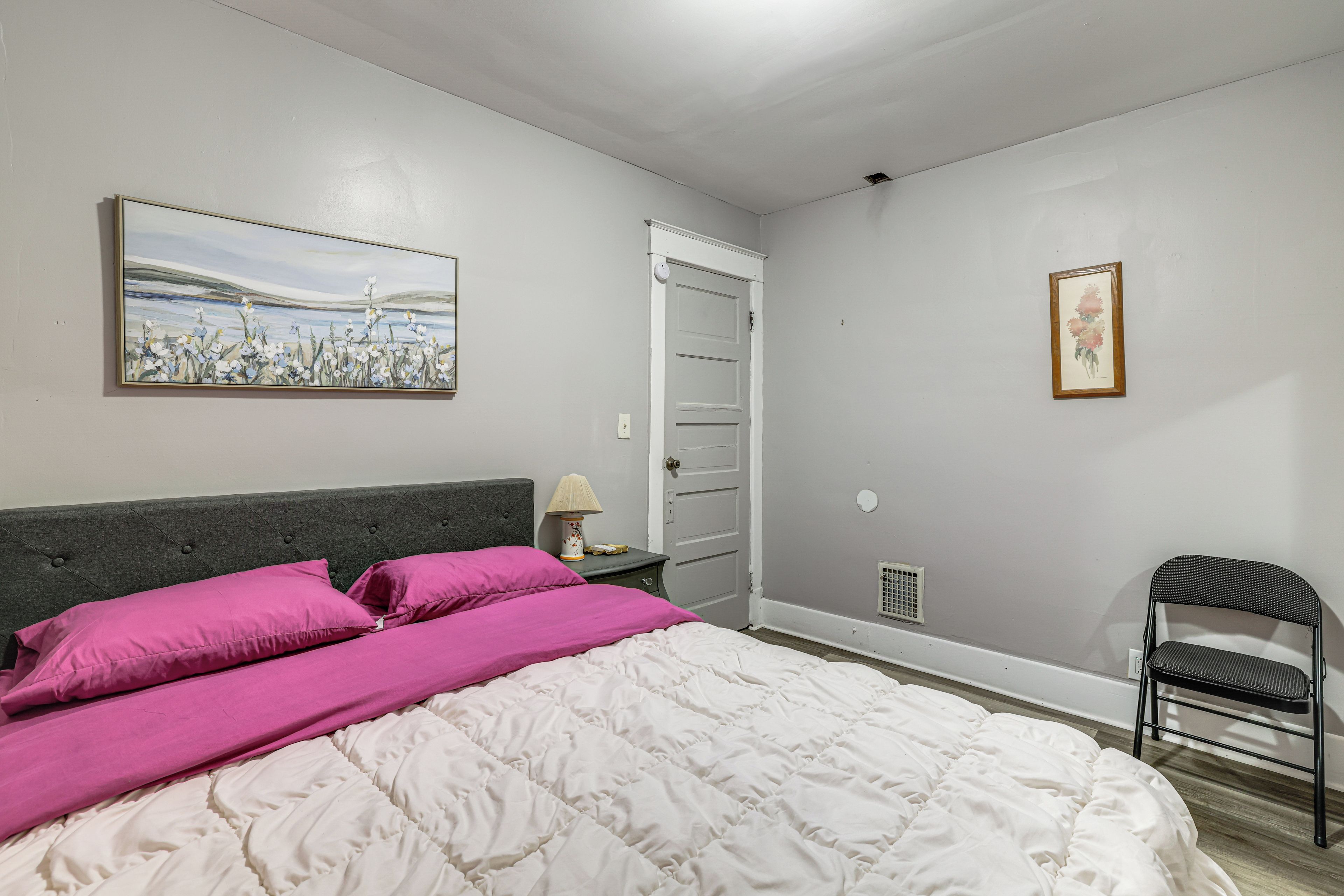 A bedroom with a bed, a nightstand, a chair, and two wall-mounted paintings.