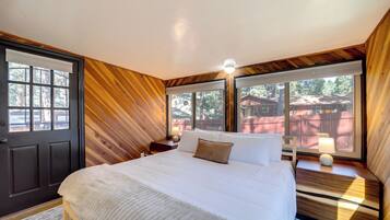 Een slaapkamer met een groot bed, houten wanden en uitzicht op het omliggende landschap.