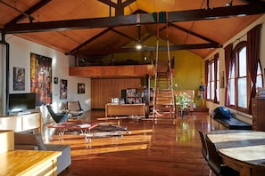 A spacious loft with high ceilings, a wooden floor, a loft bed, a dining area, and a staircase leading to an upper level. - Central City Warehouse Apartment (Melbourne)