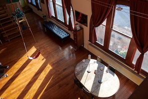Ein Zimmer mit Holzboden, einem runden Tisch mit Kerzen, einer Bank und Blick durch große Fenster.