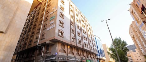 A multi-story hotel with a prominent entrance, a ground-level shop, and a parking area.