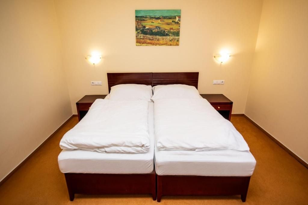 Un lit double avec une tête de lit en bois, deux tables de chevet et des lampes fixées au mur.