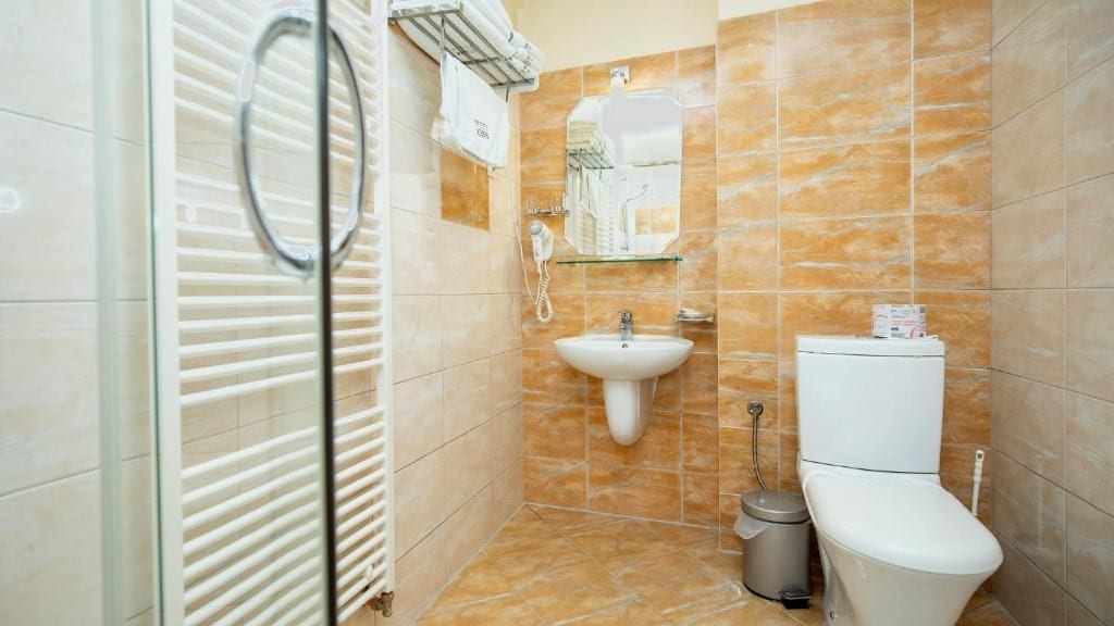 A bathroom with a glass shower enclosure, a sink, a toilet, and a trash bin.