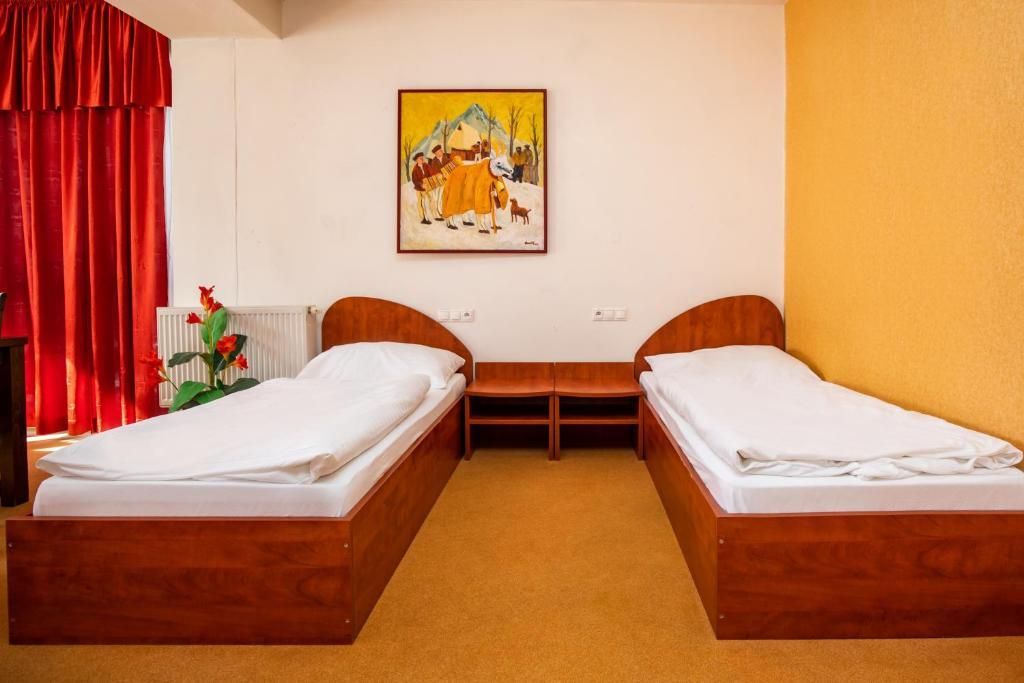 A room with two wooden beds, a small table, and a painting on the wall.