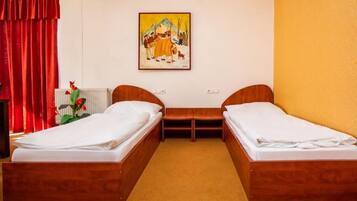 A room with two wooden beds, a small table, and a painting on the wall.