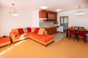 Una sala de estar moderna con un sofá seccional, una zona de comedor con una mesa y sillas de madera, y una cocina con armarios de madera y un ventanal.