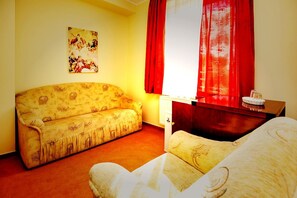 A room with a sofa, a small table, a lamp, and a painting on the wall.