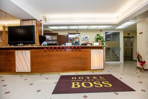Balcão de recepção de hotel com televisão de tela plana, um armário de madeira e uma área de recepção com um mapa-múndi na parede.