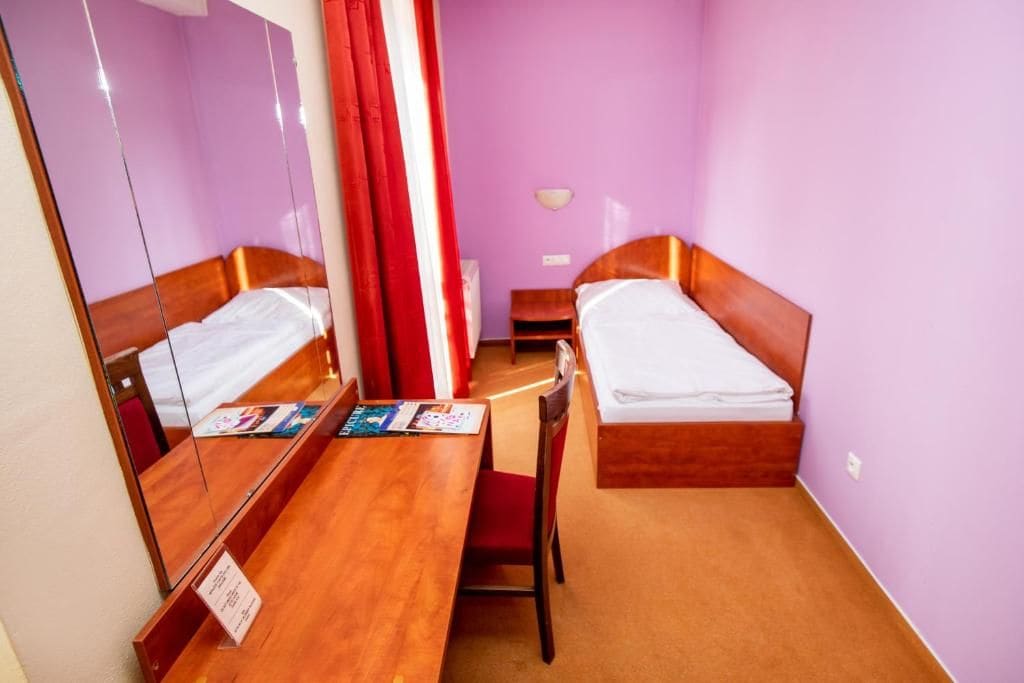 Una habitación de hotel con dos camas, un escritorio de madera, un espejo y una cortina roja.