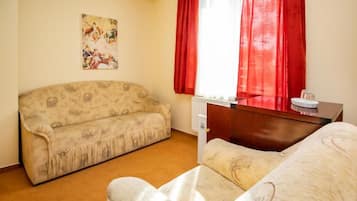Une pièce avec un canapé, un lit, une fenêtre avec des rideaux rouges et un radiateur.
