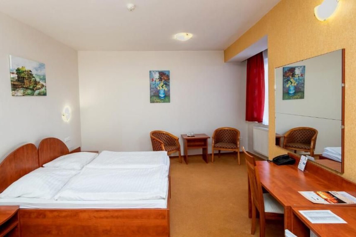 Una habitación de hotel con una cama, dos sillones, un escritorio y un espejo.