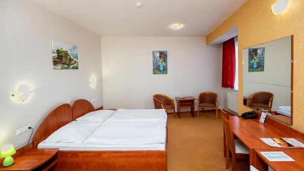 A hotel room with a bed, two chairs, a desk, and a mirror.