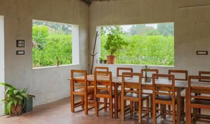 Zona pranzo con tavolo e sedie, ampie finestre vista sul verde e una pianta in vaso sul davanzale.
