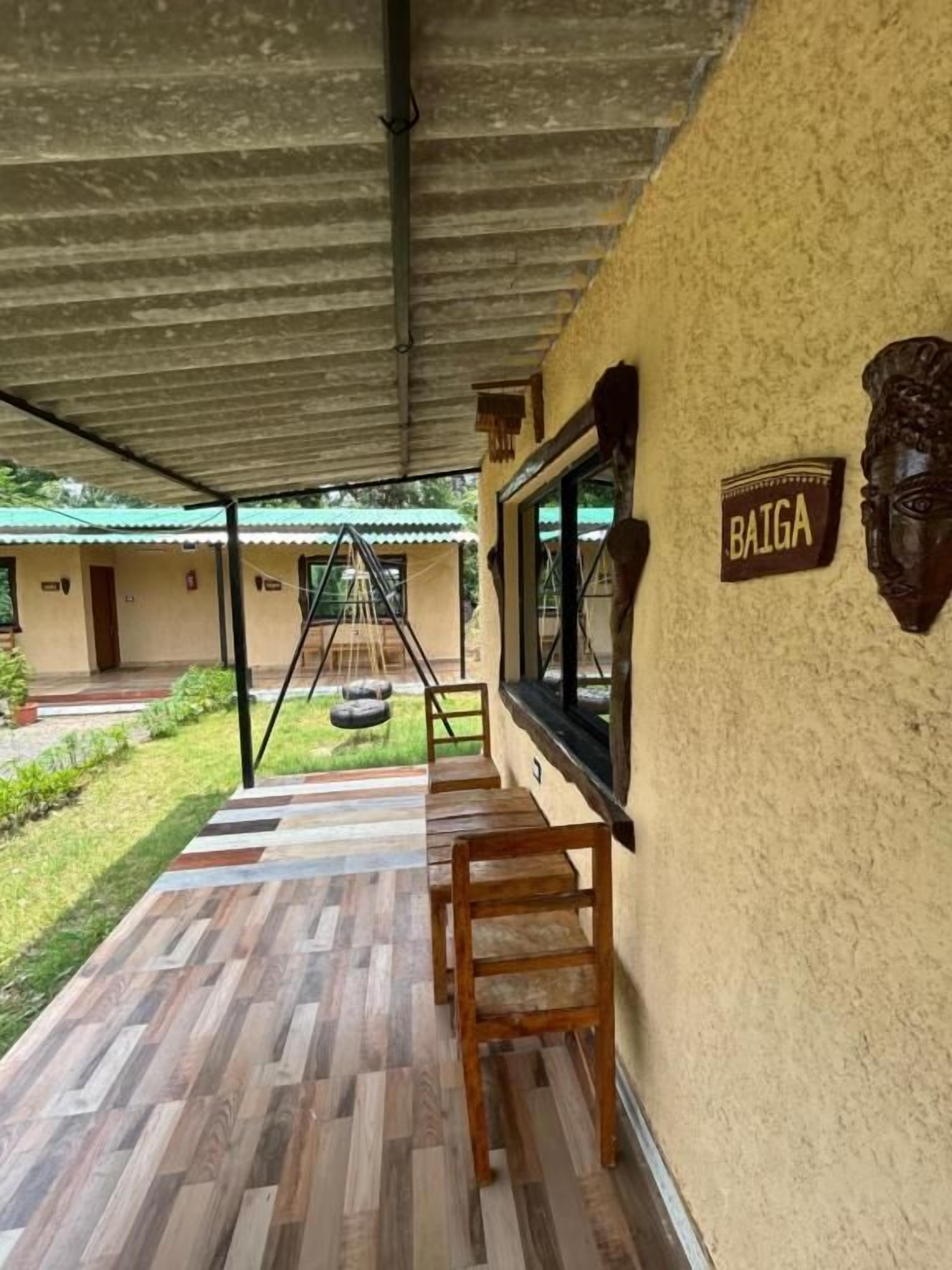 An outdoor seating area with a wooden bench and a table, a sign reading 'BAIGA', and a view of a building in the background.