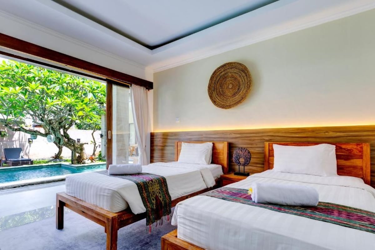 A hotel room with two beds, a view of a swimming pool, and a large woven wall art piece.