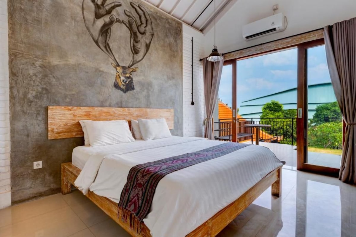A bedroom with a large bed, a wooden headboard, a ceiling fan, and a view of the outdoors.