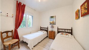 Una camera da letto con due letti singoli, una sedia in legno, un comodino e una finestra con tende.