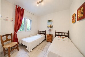 Ein Schlafzimmer mit zwei Einzelbetten, einem Holzstuhl, einem Nachttisch und einem Fenster mit Vorhängen.