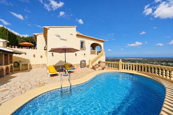Ein Poolbereich mit freiem Blick auf Villa Ventura, mit einem geschwungenen Pool und einer Terrasse mit Liegestühlen und Sonnenschirm.