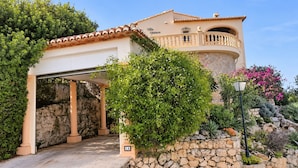 Una villa con facciata in pietra, ingresso coperto e un balcone con ringhiera.