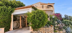 Eine Villa mit Natursteinfassade, einer überdachten Eingangspforte und einem Balkon mit Geländer.