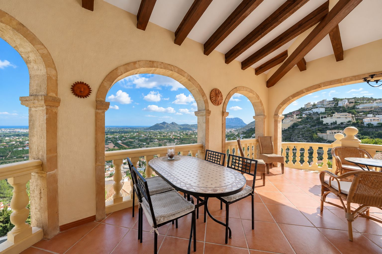 Eine Terrasse mit Tisch und Stühlen, mit Blick auf eine malerische Landschaft mit Hügeln und Gebäuden.