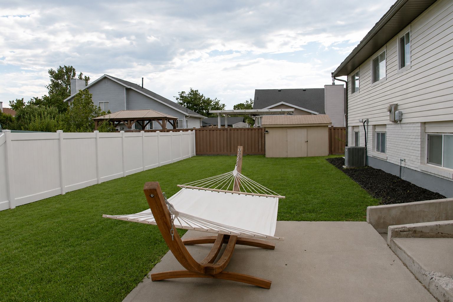 A hammock on a concrete patio with a white fence and a house in the background.