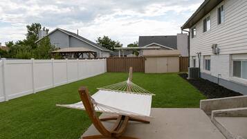 A hammock on a concrete patio with a white fence and a house in the background.