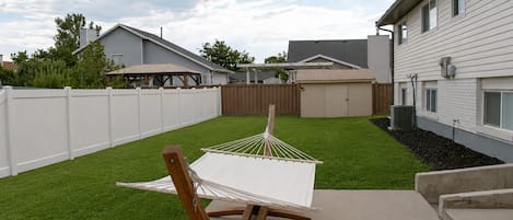 A hammock on a concrete patio with a white fence and a house in the background.