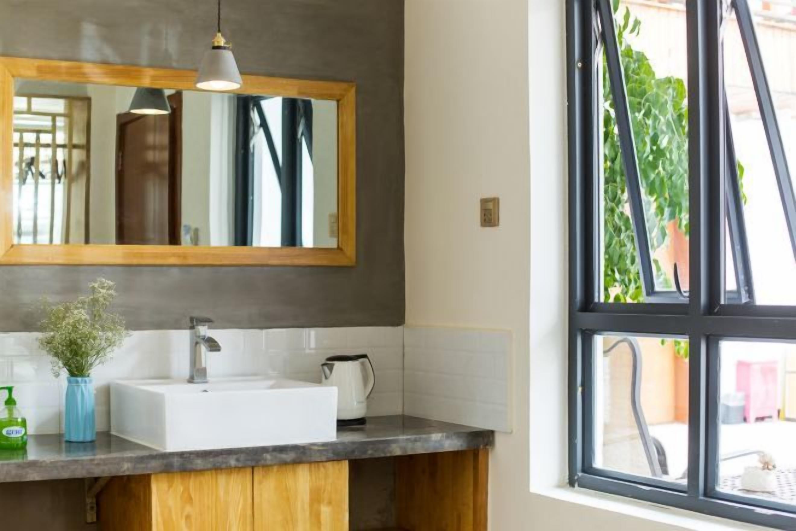 A bathroom with a large mirror, a white sink, a wooden vanity, and a window with a view of greenery.