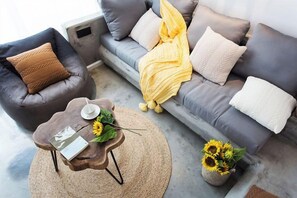 Un salón moderno con un sofá gris, un sillón marrón y una mesa de centro redonda con un libro y un jarrón de girasoles.