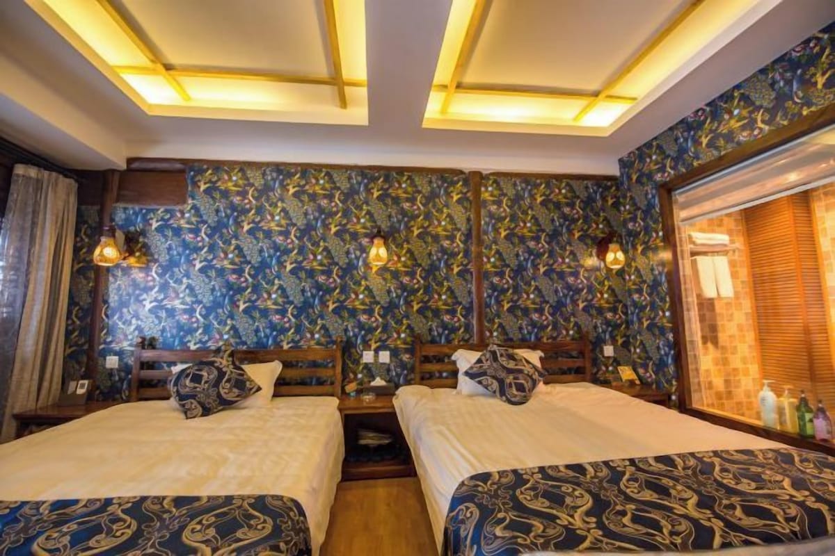 Habitación de hotel con dos camas, un papel tapiz estampado y una ventana con persianas.