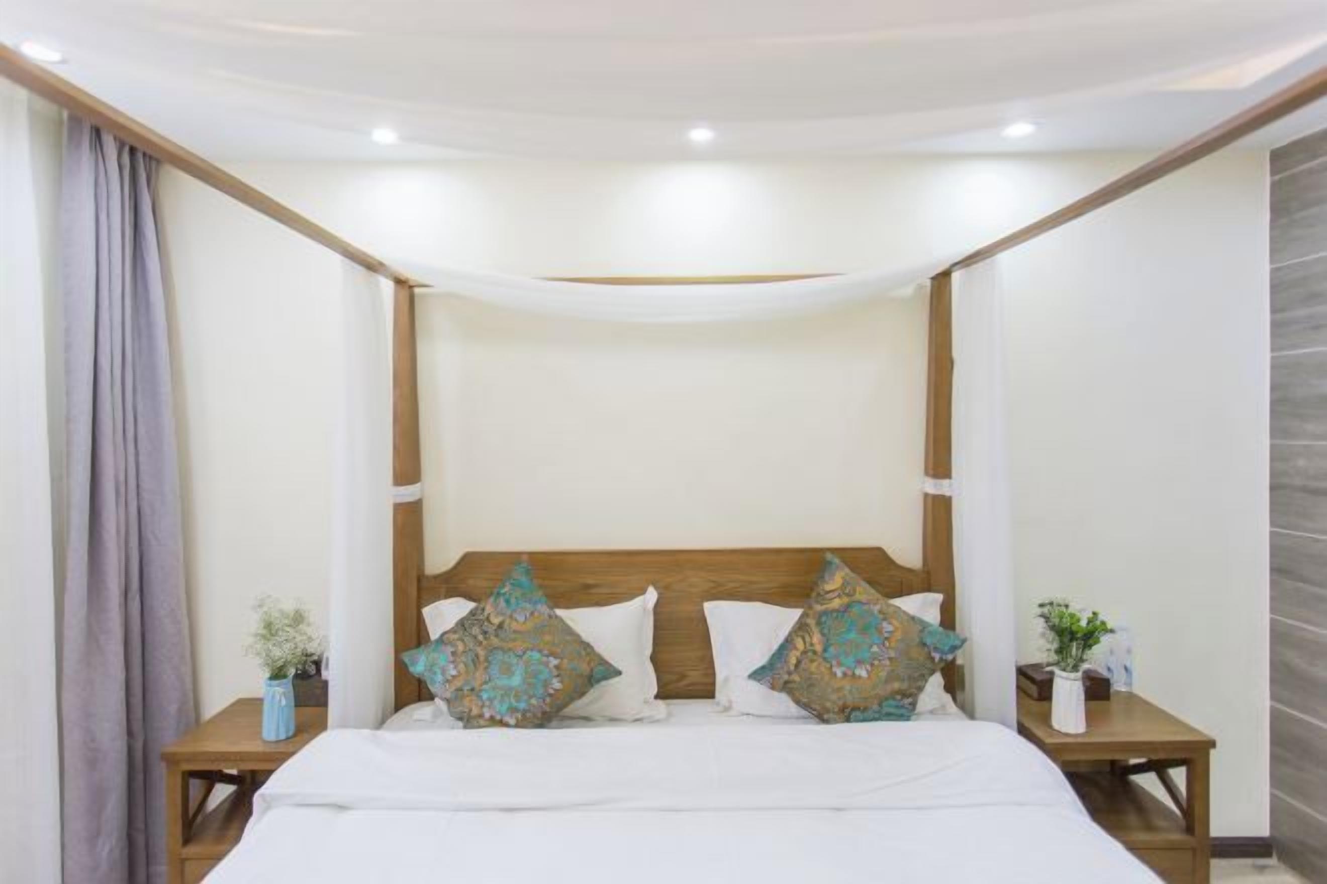 A bedroom with a canopy bed, wooden headboard, two bedside tables with decorative pillows, and a nightstand with a plant.