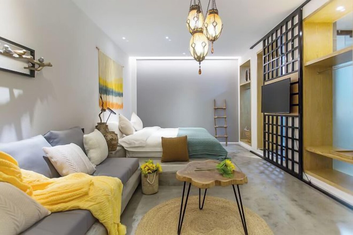 Una sala moderna con sofá, una mesita de centro y cojines decorativos. Hay un televisor sobre un mueble bajo y un aparador de madera.