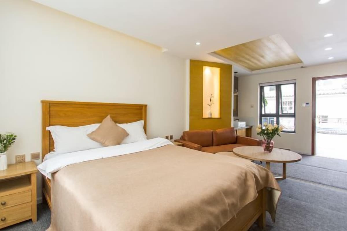 Habitación de hotel con una cama, mesita de noche, lámpara y una pequeña mesa redonda con un florero.