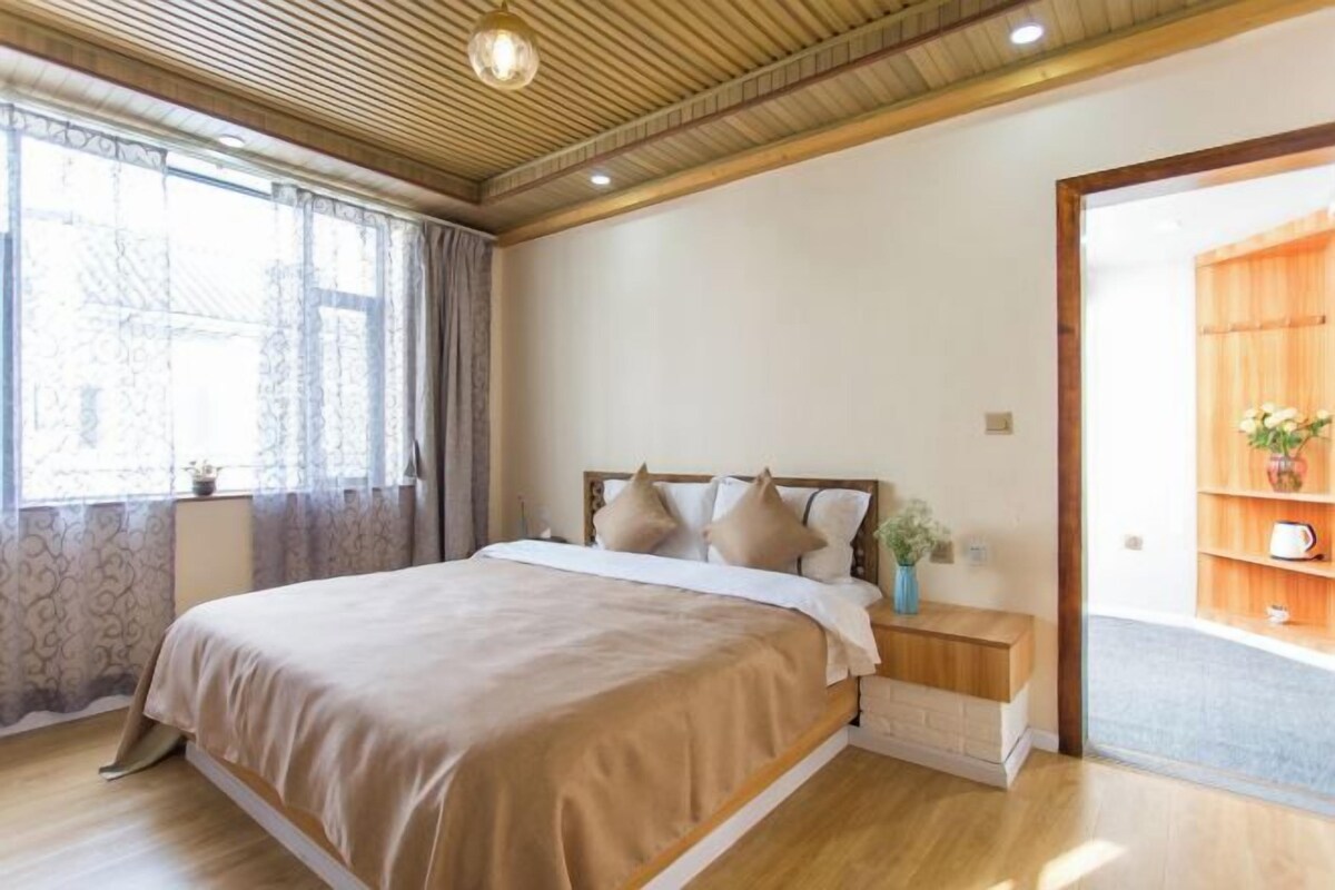 Un dormitorio con una cama grande, mesitas de noche, una ventana con cortinas y techo de madera.