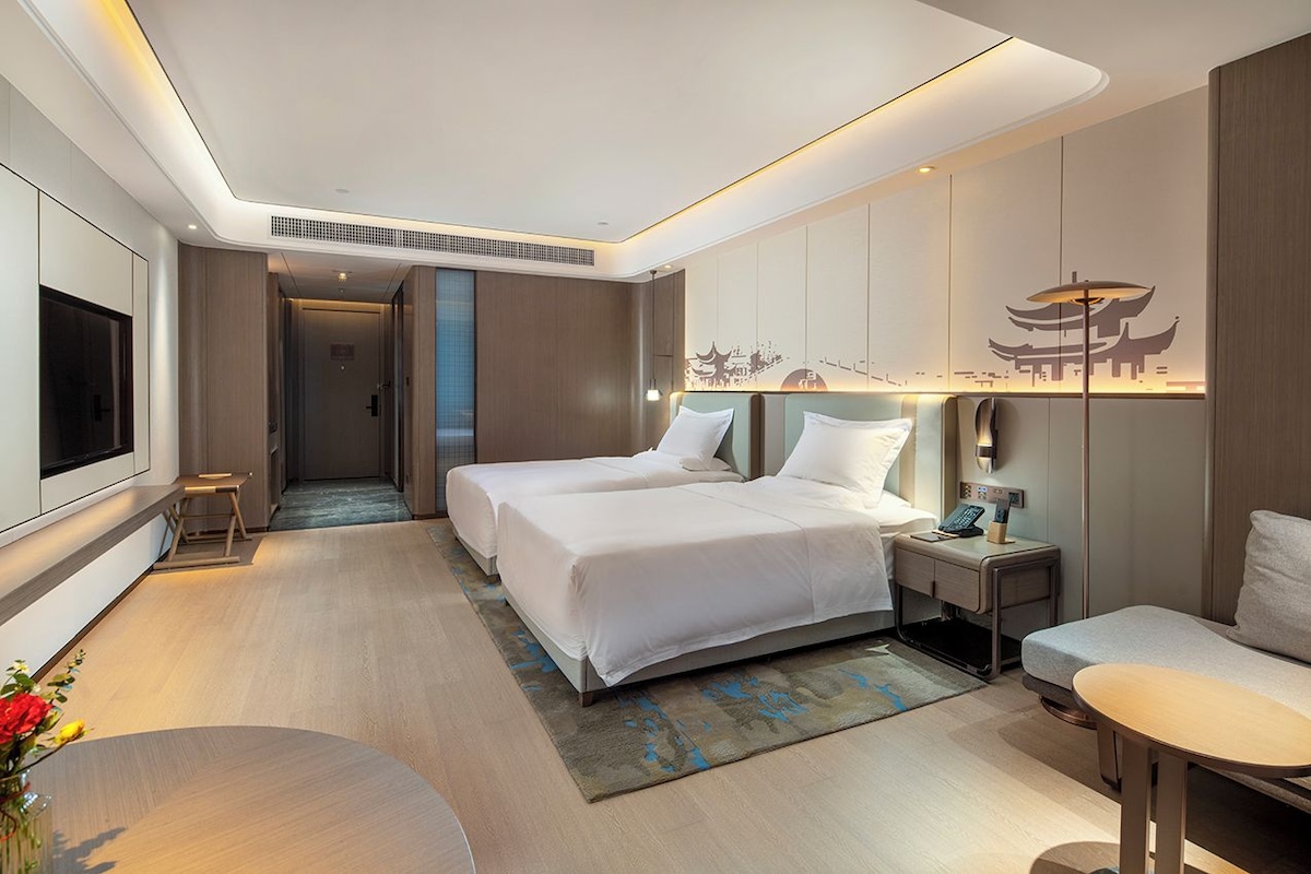A modern hotel room with a large bed, bedside tables, a TV, and a decorative wall.