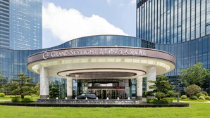 A modern hotel with a curved entrance, surrounded by lush greenery and tall buildings.