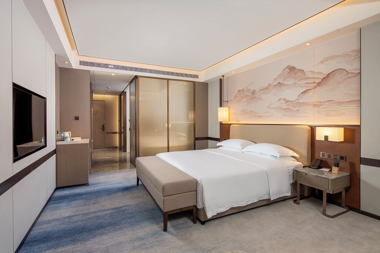 Una habitación de hotel con una cama grande, mesita de noche y televisión.