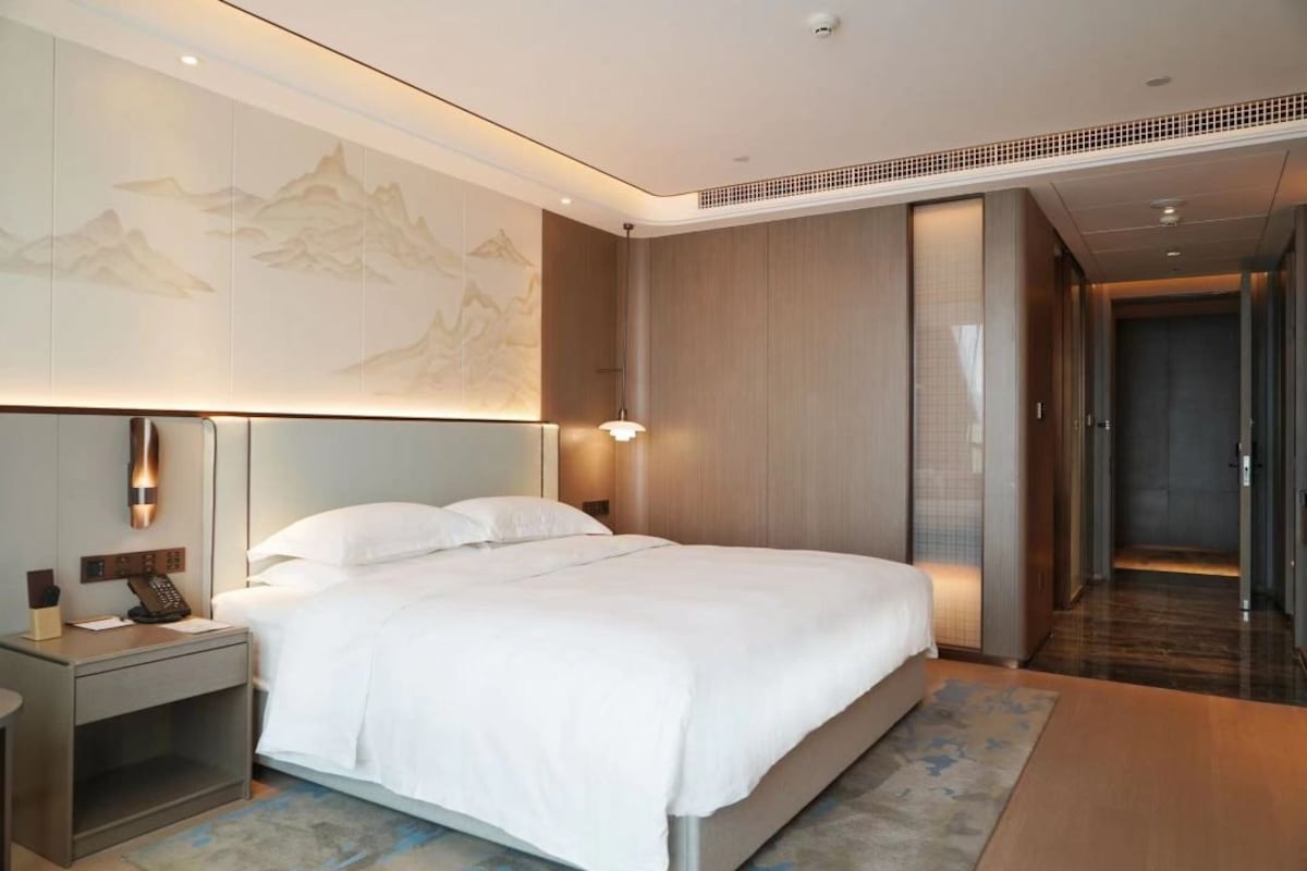 Une chambre d’hôtel avec un lit, une table de chevet, une lampe fixée au mur et un grand tableau.