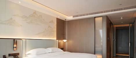 A hotel room with a bed, nightstand, wall-mounted lamp, and a large painting.