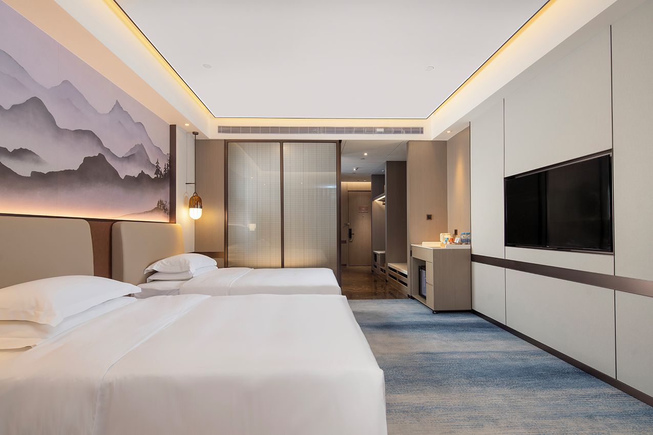A hotel room with two beds, a TV, a desk, and a bathroom.