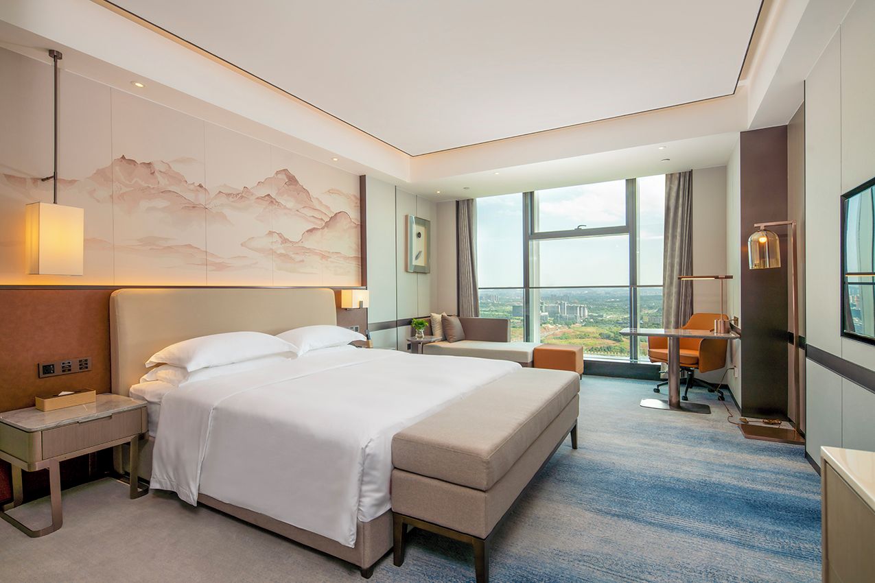 Een hotelkamer met een groot bed, een bureau, een stoel en uitzicht op de stad.