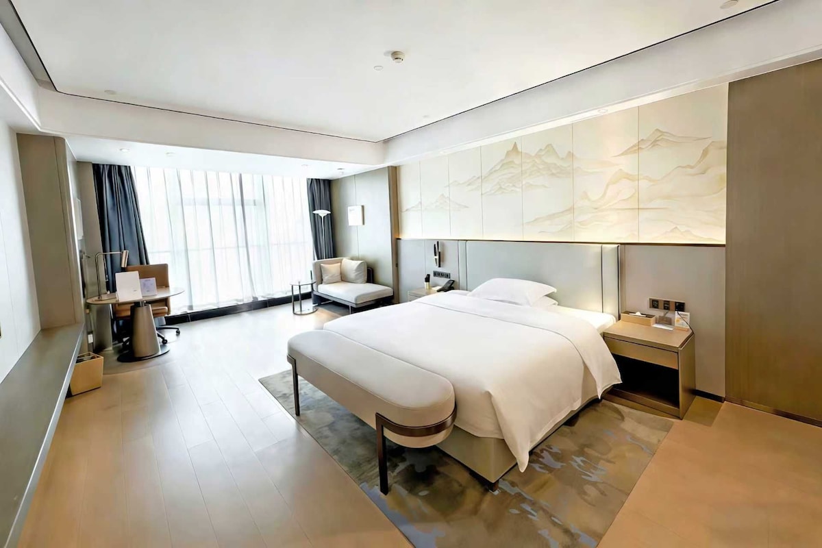 Et moderne hotelværelse med en stor seng, et skrivebord, en stol og udsigt til bjergene gennem vinduet.
