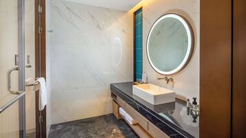 A modern bathroom with a marble floor, a round mirror, a sink, and a glass shower enclosure.