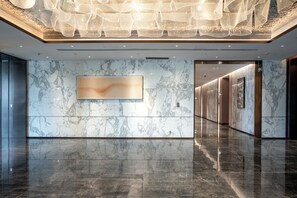 A modern lobby with marble walls, a reflective floor, and a contemporary light fixture.