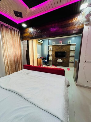 A bedroom with a bed, a desk, a chair, a TV, and a fan. - Privacy and comfort our first priority (Lucknow)